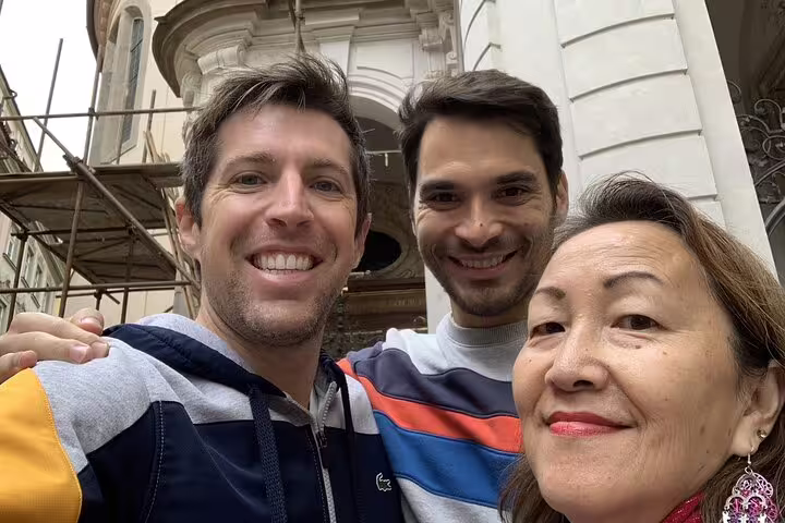 Three smiling tourists posing for a selfie in front of a historic building in Prague Old Town