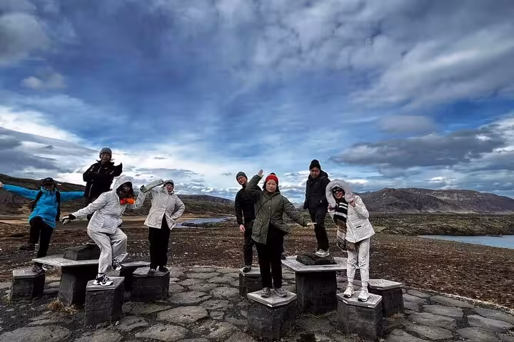 Group of tourists posing on stone pedestals with Snaefellsnes Peninsula landscape and dramatic sky behind
