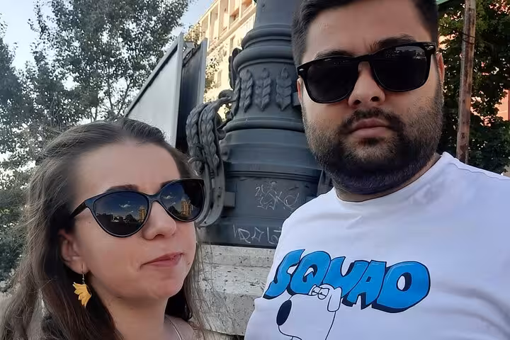 Two tourists wearing sunglasses posing near a Soviet-era monument in Bucharest
