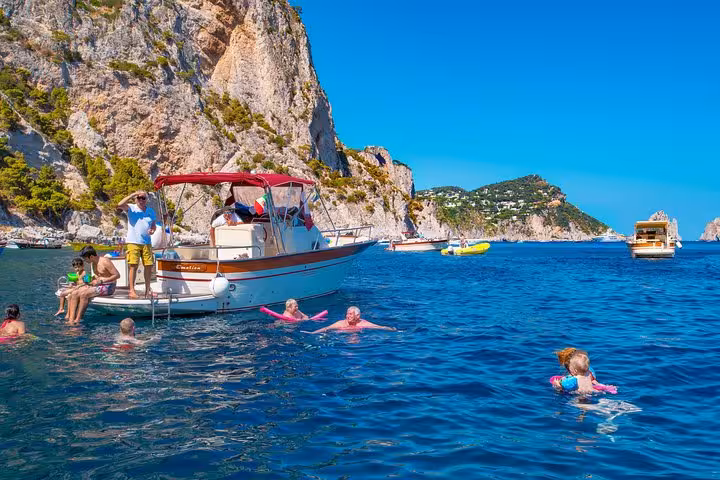 Tourists swimming around a boat near Capri's dramatic cliffs, enjoying a refreshing stop on a Positano transfer tour.