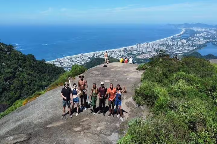 Group of tourists posing on a rocky viewpoint, overlooking Rio de Janeiro's coastline and vibrant cityscape from Tijuca Rainforest.