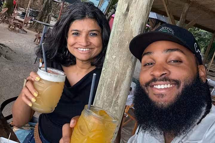 Smiling tourists enjoying tropical drinks at a beachside bar during a private Mahe Island tour.