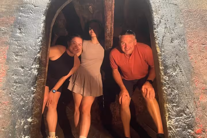 Three smiling tourists posing inside a rustic wine cellar barrel opening during a Douro Valley full-day wine tour from Porto.