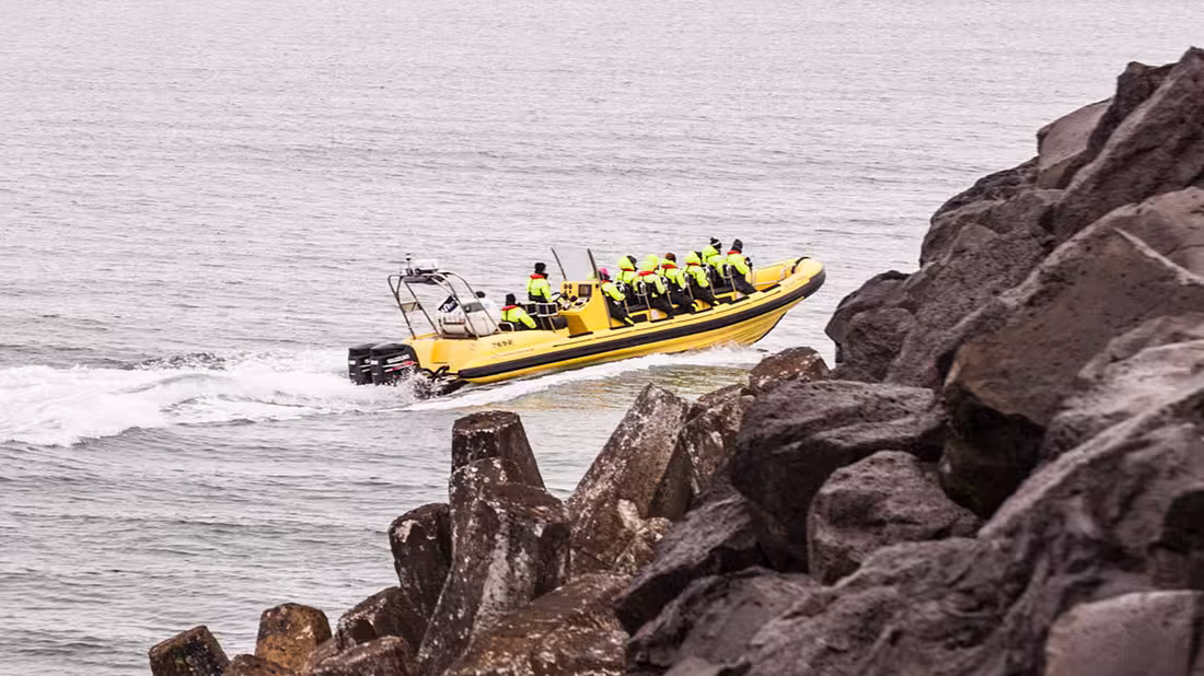 Group of tourists in a yellow RIB with rocks in foreground