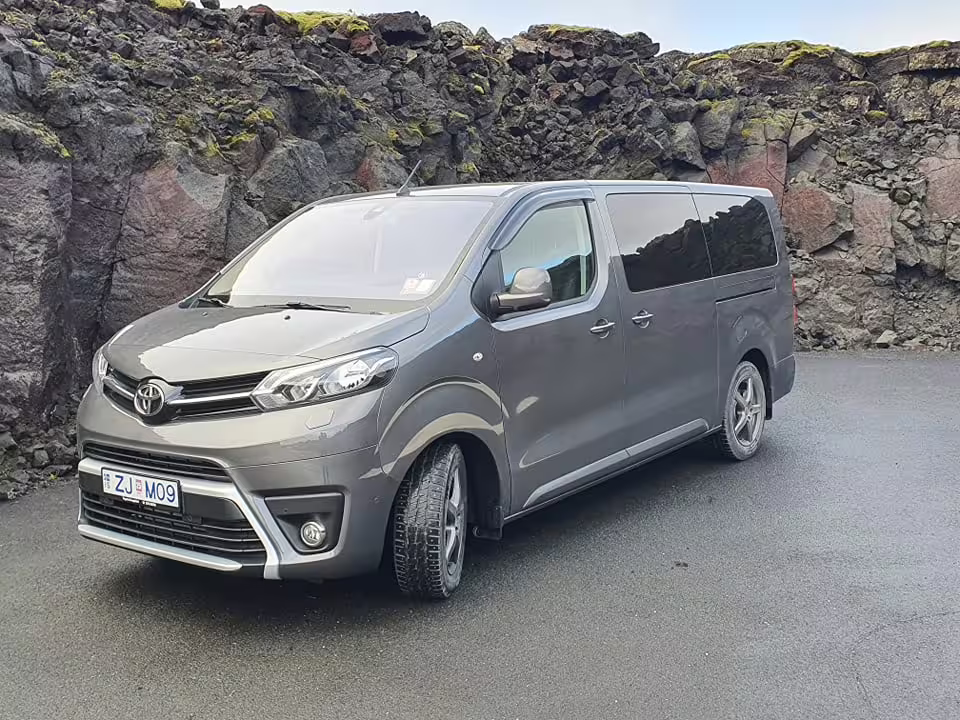 Gray Toyota Proace minivan for private airport transfer parked near volcanic rock wall in Iceland