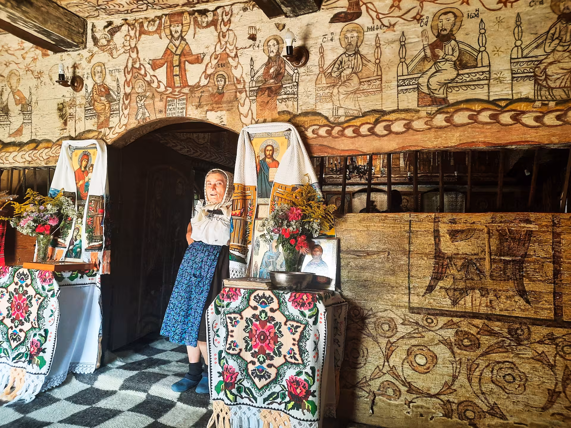 Local woman in traditional dress inside a UNESCO wooden church with ancient frescoes in Maramures Romania