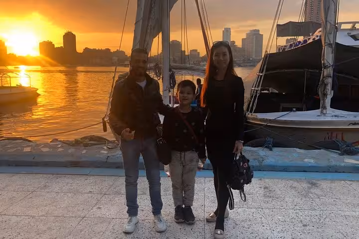Guests posing by a traditional felucca at sunset on the Nile River in Cairo with skyline views