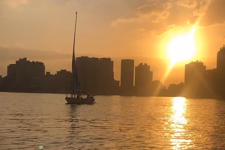 Traditional felucca sailing on the Nile River in Cairo at sunset, golden reflections with city skyline view