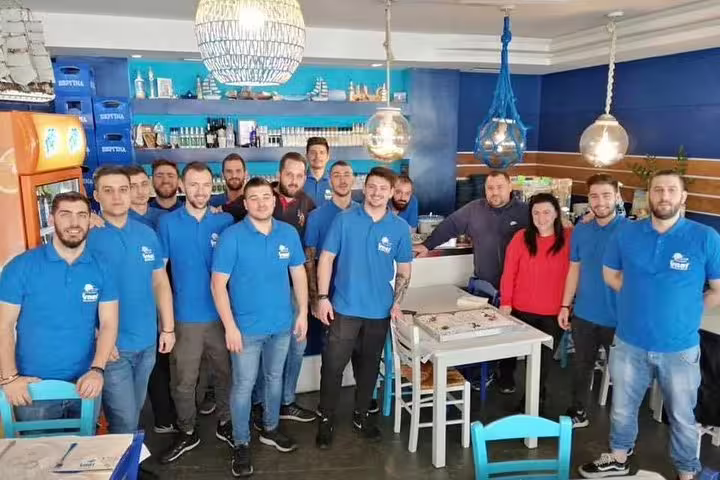 Friendly restaurant staff in a traditional local taverna dining room, welcoming guests for a grill meat experience