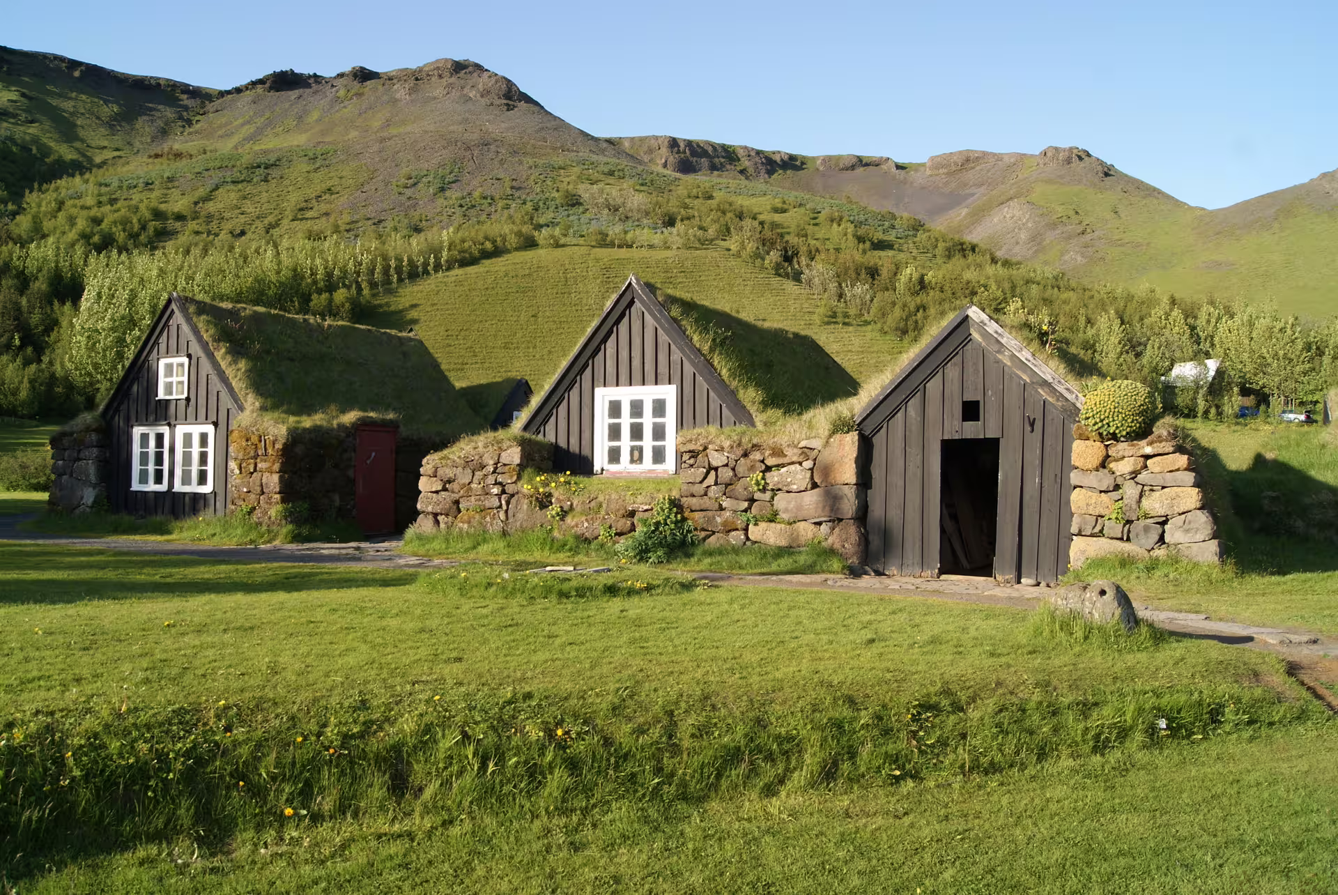 Traditional Icelandic turf houses with grass roofs against green mountains in South Iceland