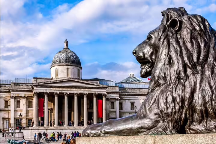 Bronze lion statue at Trafalgar Square with National Gallery columns and dome in London