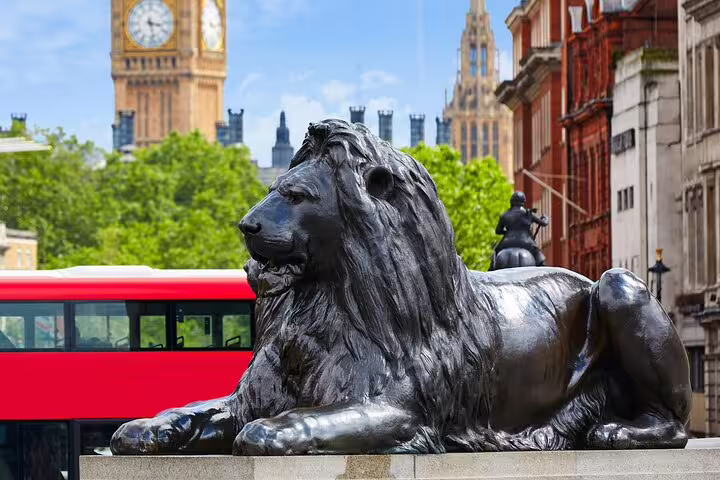 Bronze lion statue at Trafalgar Square with Big Ben and red double-decker bus in background, Westminster London