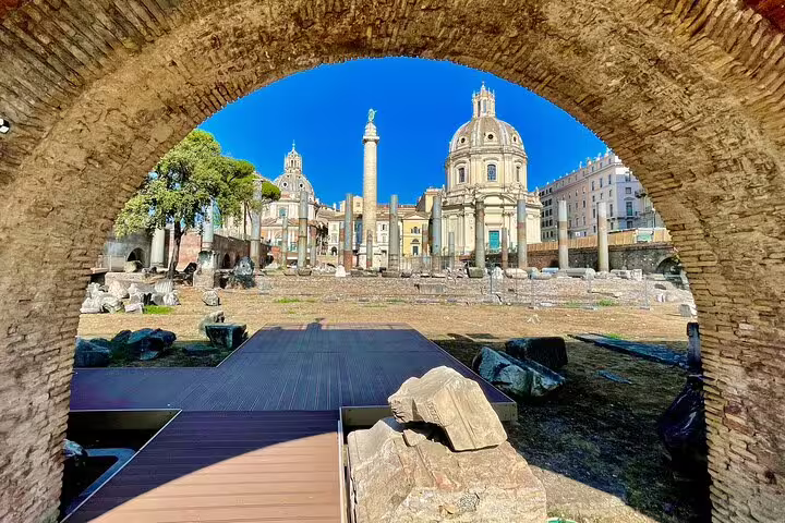 Ancient archway framing Trajan’s Column and baroque churches in the Roman Forum on a guided Colosseum panoramic tour