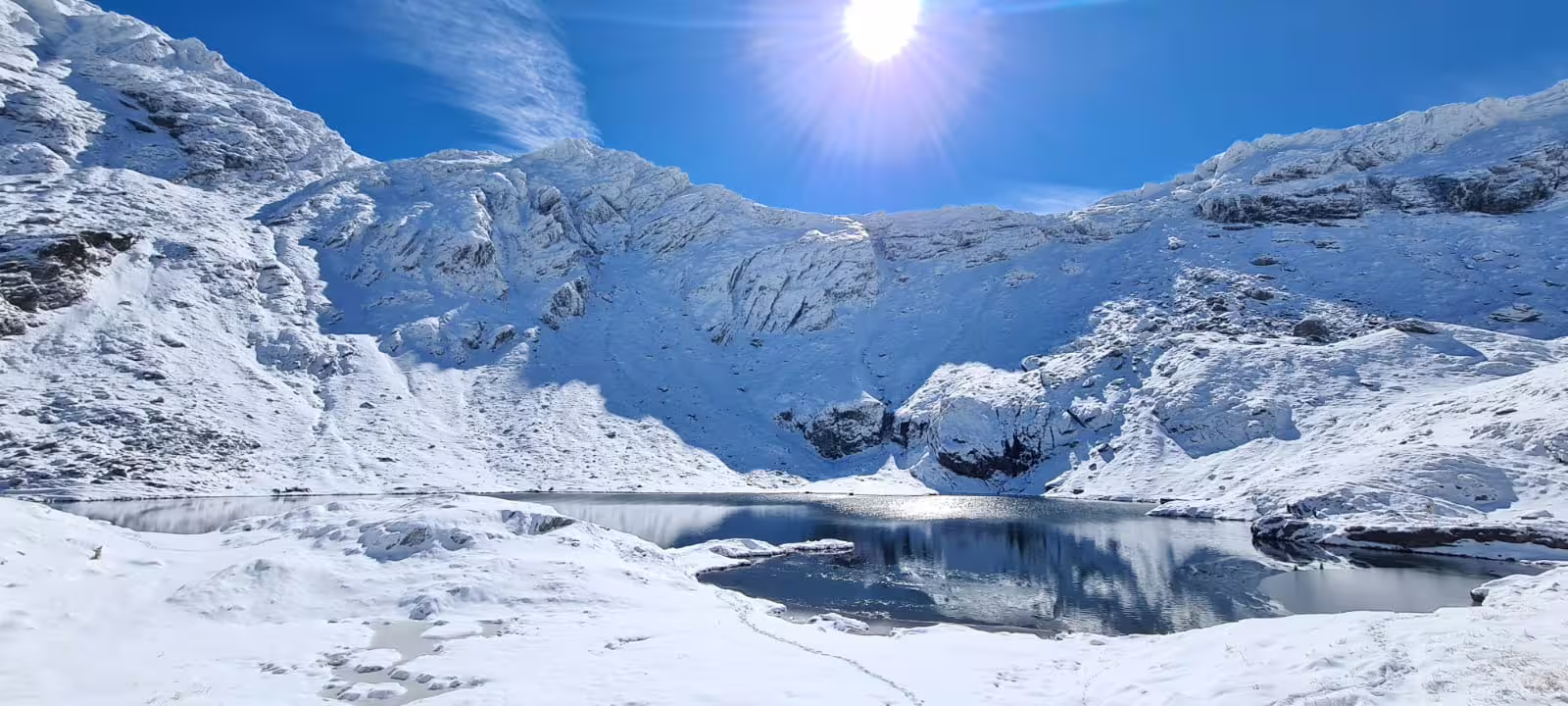 Snow-covered mountain lake reflecting blue sky and glacial peaks on a sunny winter day