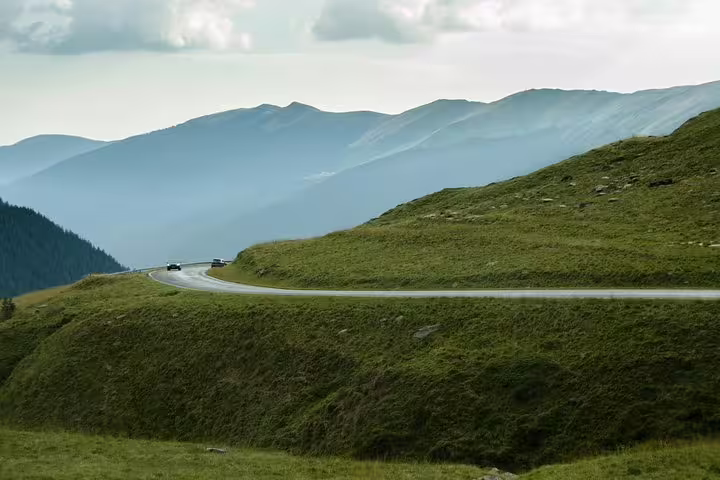 Winding Transfagarasan Road curving through green mountain slopes with misty peaks in background
