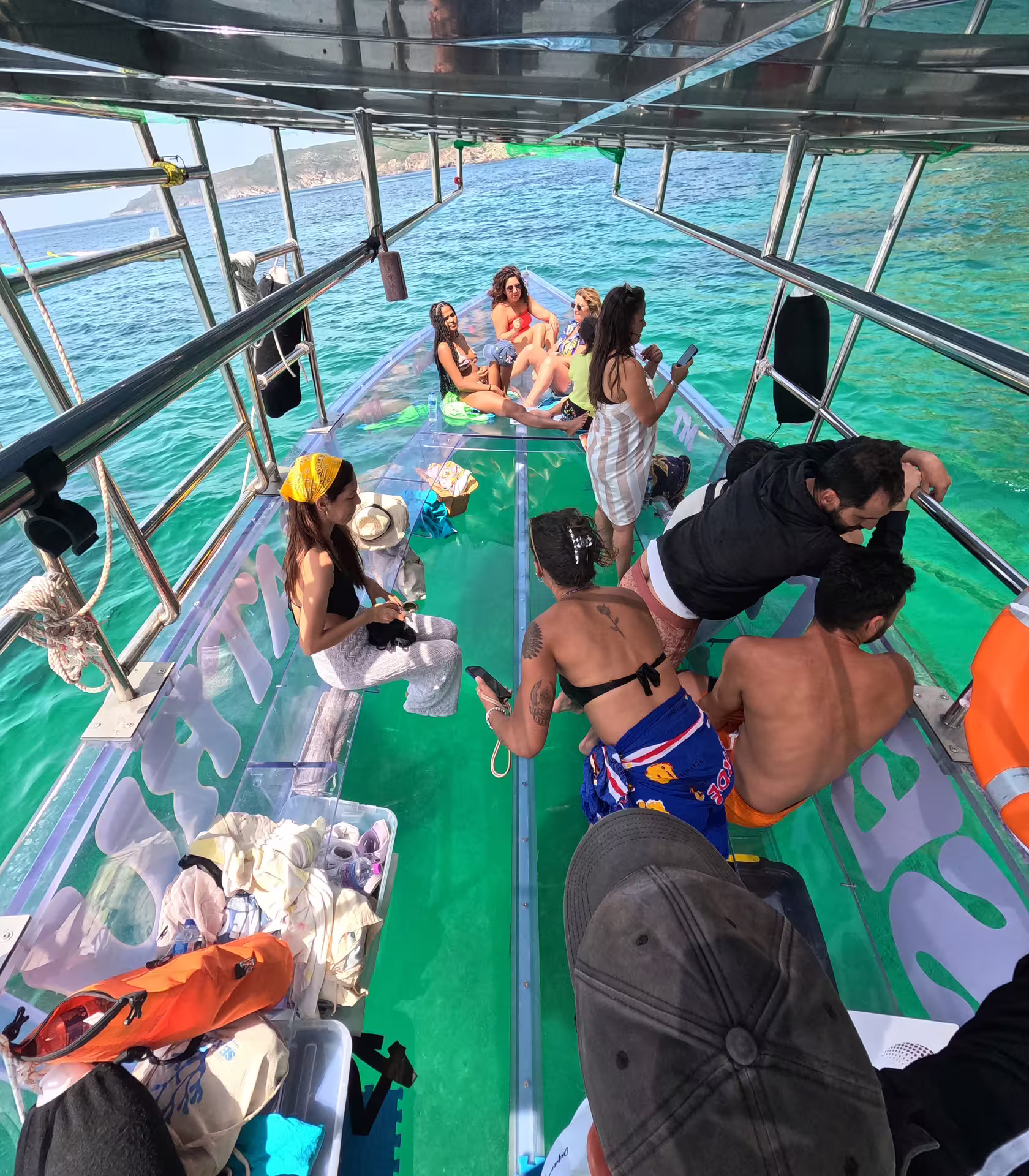 Tourists relaxing and taking photos on a transparent boat in the crystal-clear waters of Sesimbra.