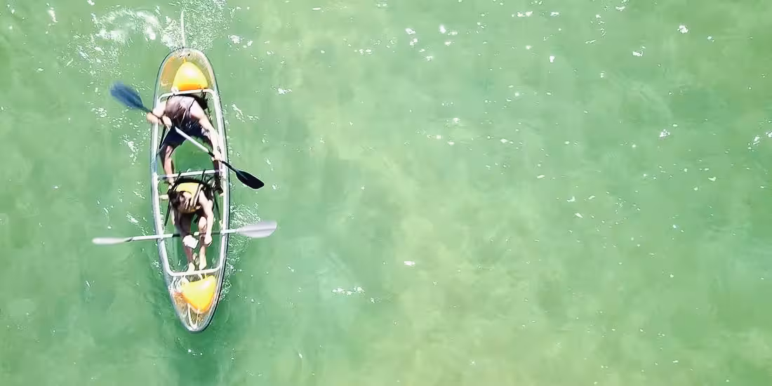 Top-down view of two people paddling a transparent kayak on clear green water during a 4-hour rental
