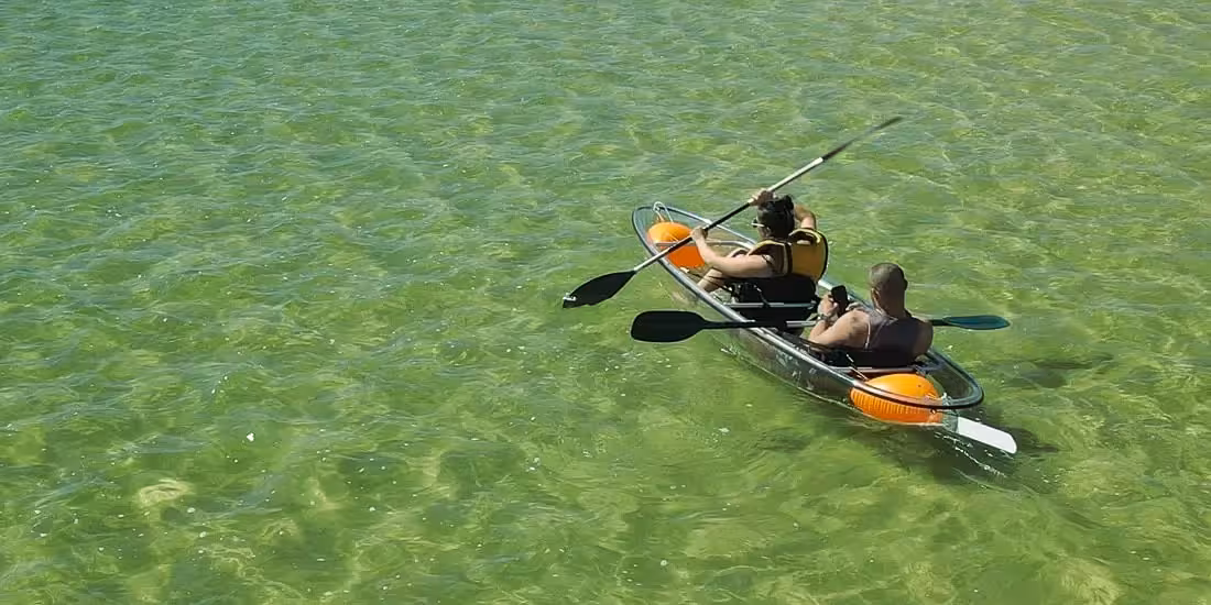 Aerial view of a clear-bottom tandem kayak gliding on shallow turquoise water on a 2-hour transparent kayak rental
