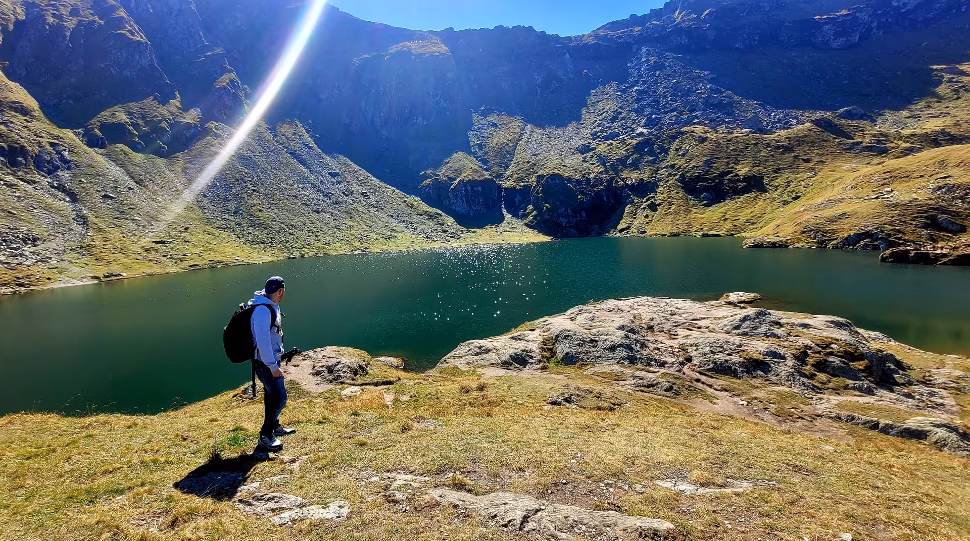 Hiker with backpack overlooking a emerald alpine lake surrounded by dramatic mountain cliffs in Transylvania