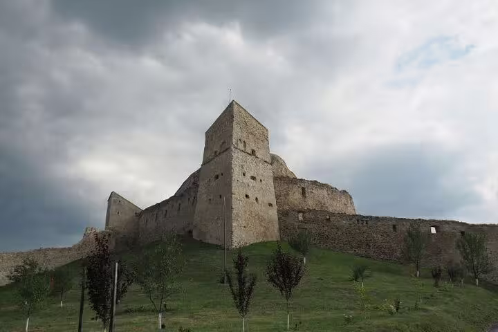 Medieval stone castle ruins on a green hilltop under dramatic cloudy skies in Transylvania