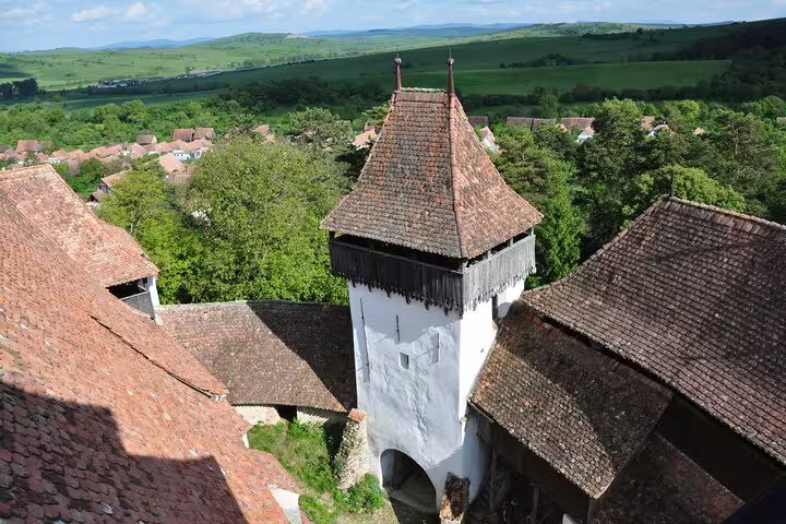 Aerial view of medieval fortified church tower with terracotta rooftops and green Transylvania hills