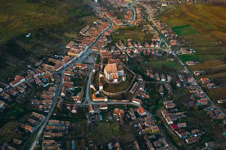 Aerial view of a medieval Transylvanian town with a fortified church surrounded by terracotta-roofed houses
