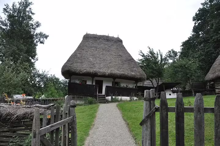 Traditional thatched-roof farmhouse with wooden fence along gravel path in rural Transylvania