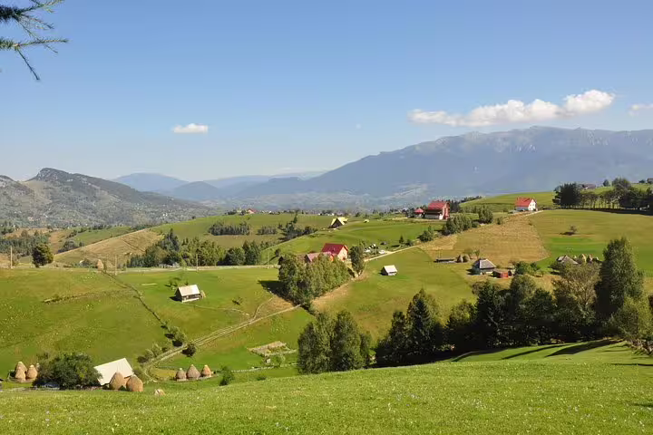Rolling green hills with traditional farmhouses and haystacks in Transylvania with Carpathian Mountains backdrop