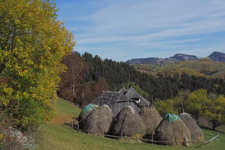 Traditional haystacks and wooden barn on green hillside in Transylvania, Carpathian Mountains in autumn