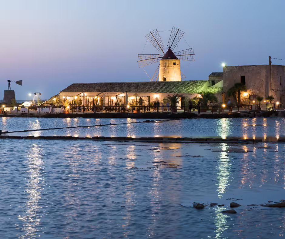 Twilight view of the illuminated Trapani salt pans and historic windmill, visited on a private tour from Palermo