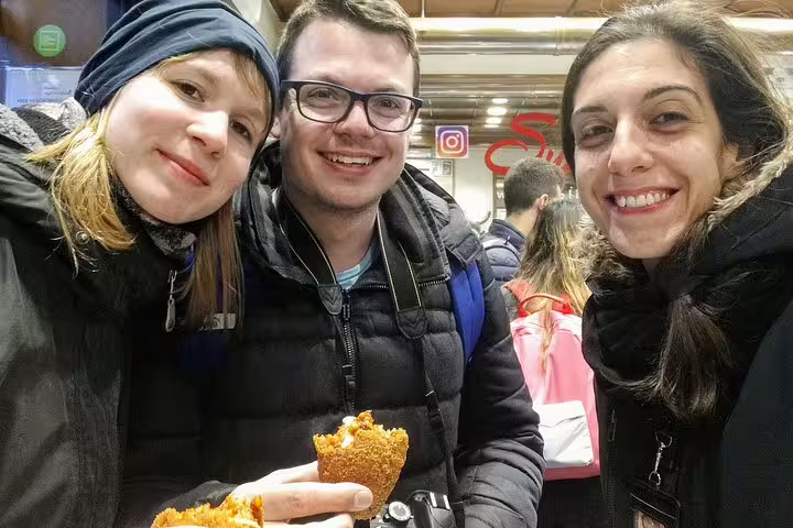 Three happy tourists savoring authentic Roman street food arancini on a Trastevere sightseeing food tour