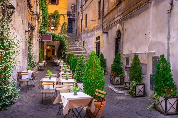 Charming cobblestone alley with outdoor restaurant tables and lush greenery in Trastevere, Rome