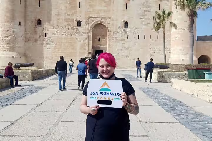 Traveler holding Sun Pyramids Tours sign at Alexandria Citadel entrance on private day tour from Cairo