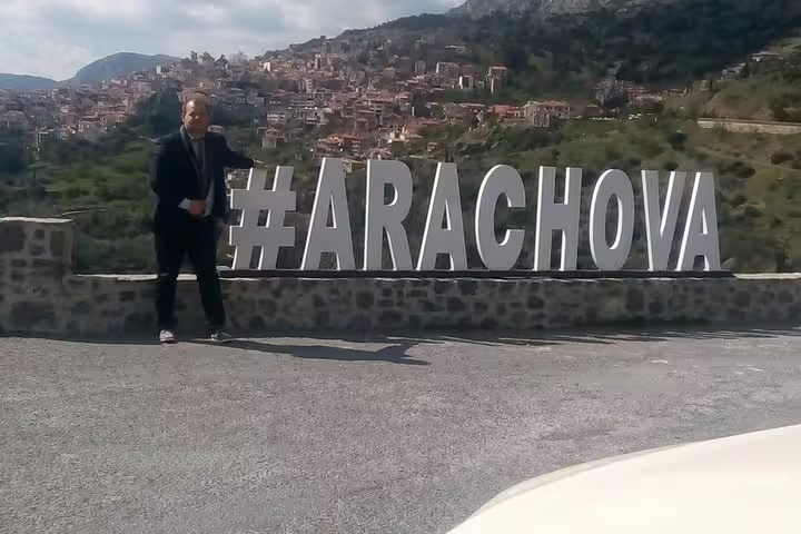 Traveler posing by #ARACHOVA sign overlooking hillside town, scenic break on Delphi Arachova Distomo tour