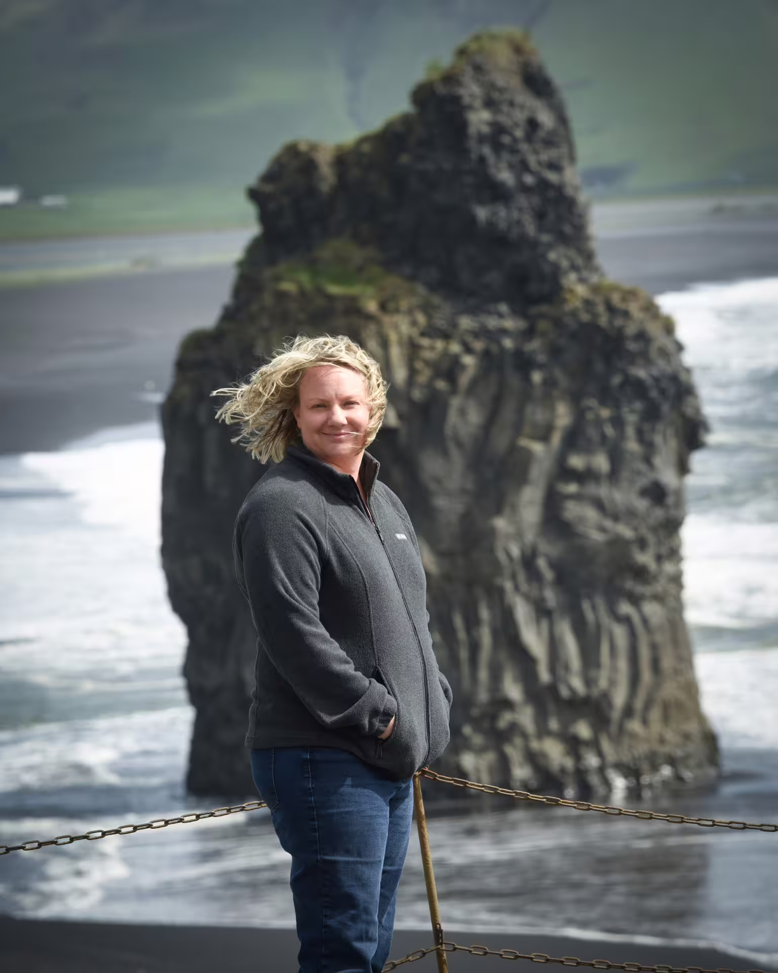 Smiling traveler posing at Iceland black sand beach with dramatic basalt sea stack on South Coast tour