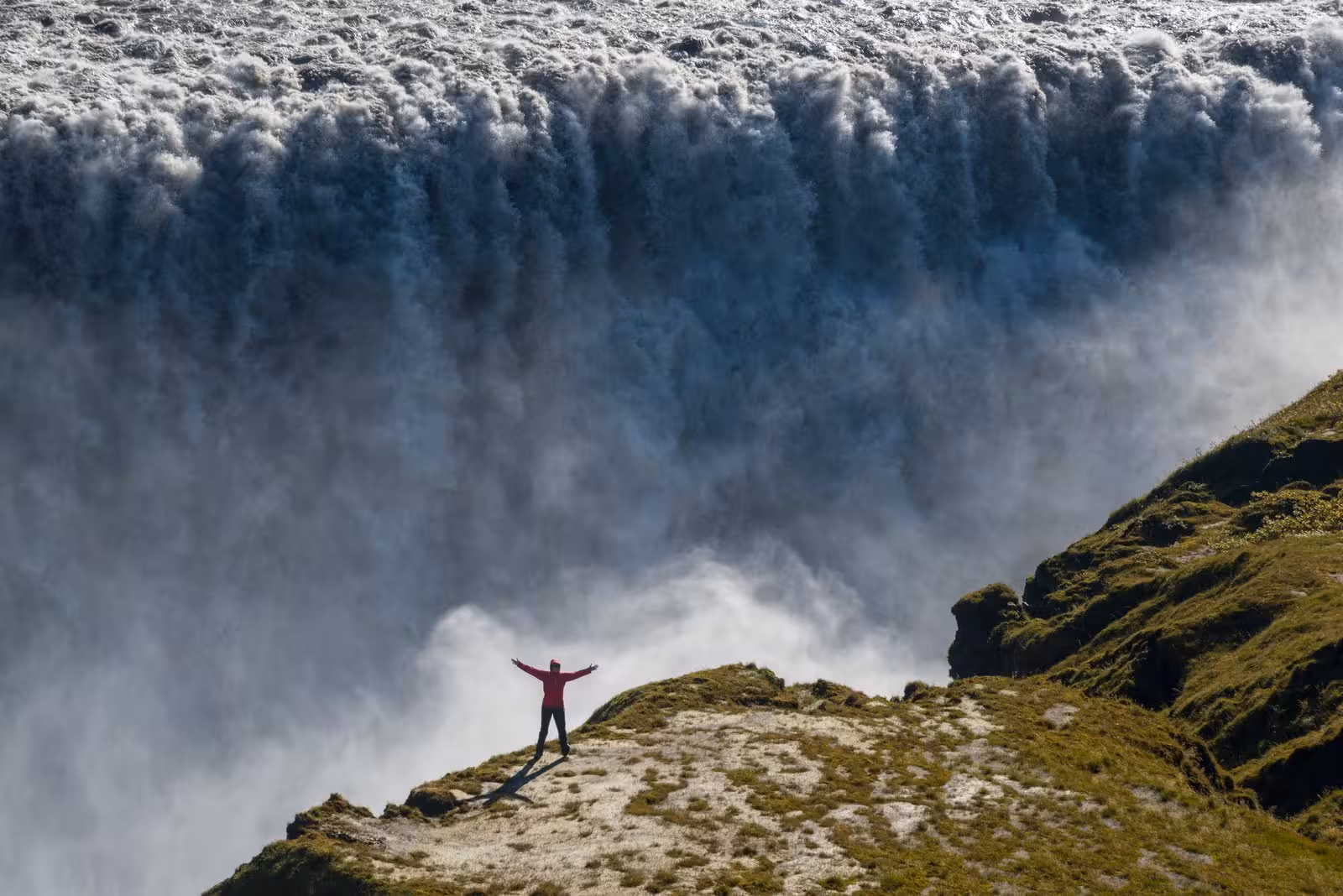 Traveler stands triumphantly near the edge of mighty Dettifoss waterfall in Iceland's scenic landscape.