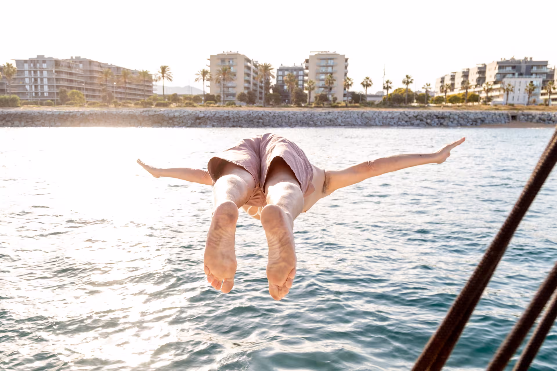 Traveler dives from boat into sparkling water on Farewell at Sea catamaran cruise near the coastline at golden hour