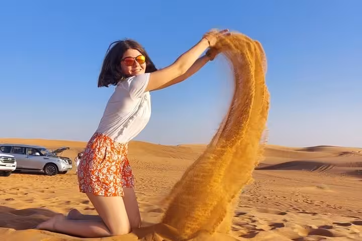 Traveler tossing sand on Dubai dunes during evening desert safari, scenic sunset desert photo stop