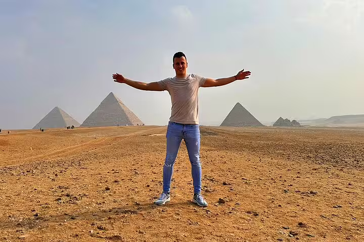 Traveler posing with arms wide at Giza Pyramids on Cairo day trip to Memphis and Saqqara, Egypt