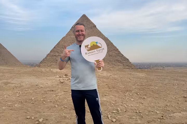 Traveler at Giza Plateau on private Pyramids and Sphinx tour, posing by Great Pyramid before camel ride