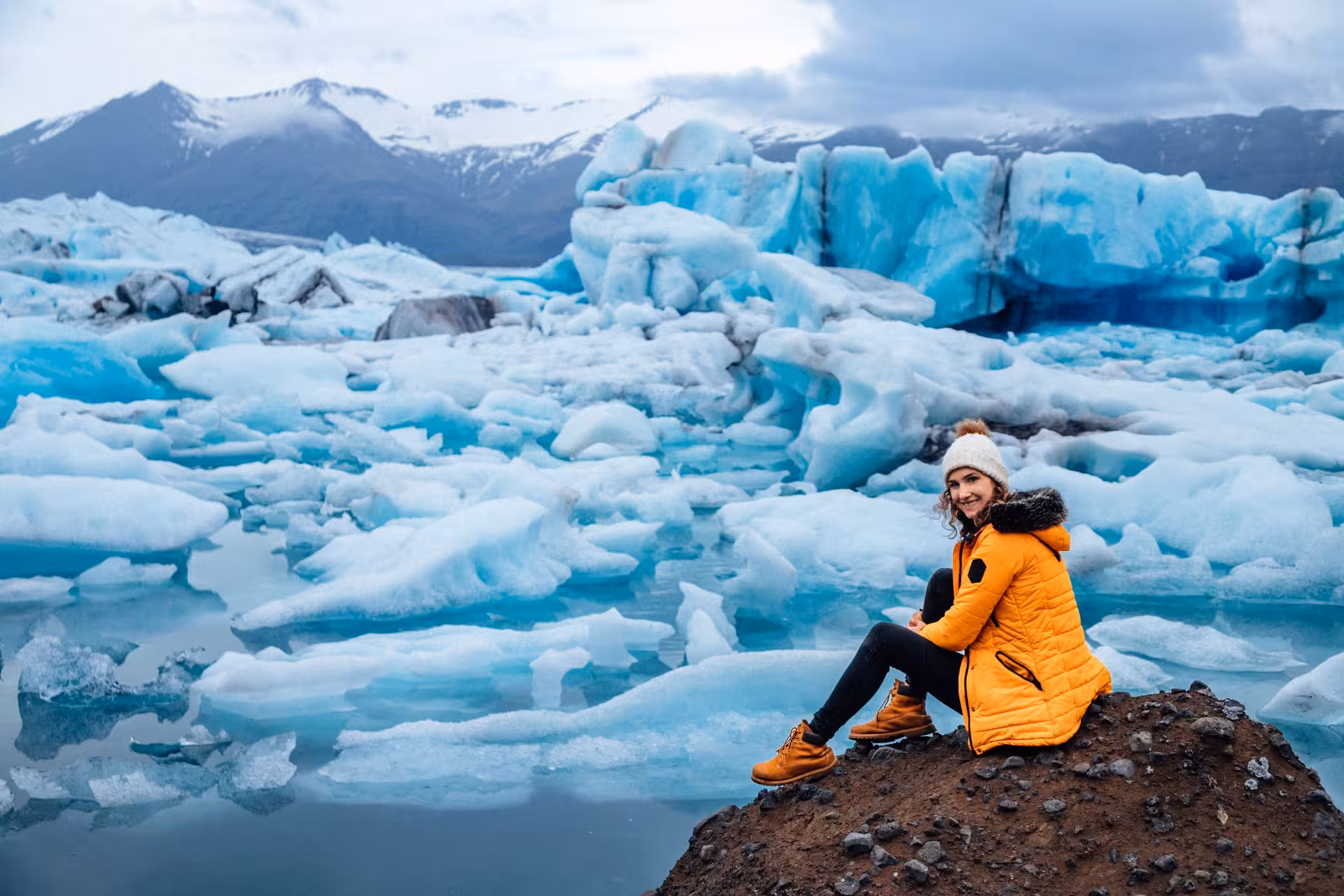 Traveler in orange jacket enjoys serene view of icy Glacier Lagoon on Northern Lights tour.