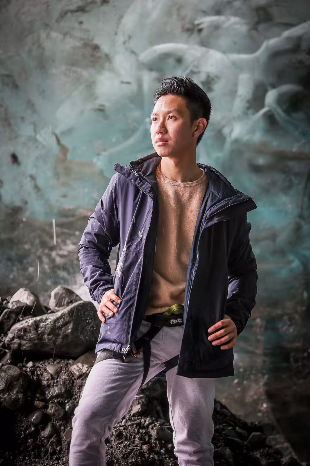 A traveler in a jacket poses inside a stunning private ice cave with vivid teal glacial ice walls behind.