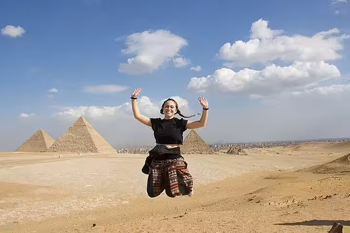 Traveler jumping with Giza Pyramids backdrop on private Alexandria port day tour, Egypt shore excursion