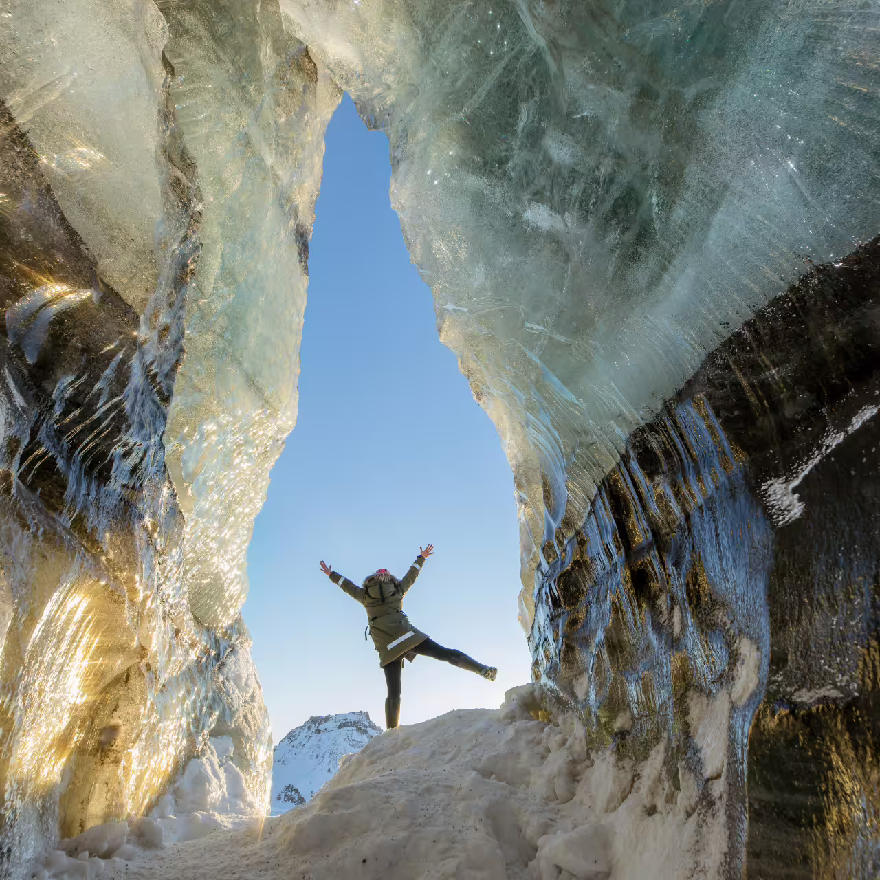 Traveler jumping joyfully at the entrance of Katla ice cave with stunning glacial walls on Iceland South Coast tour
