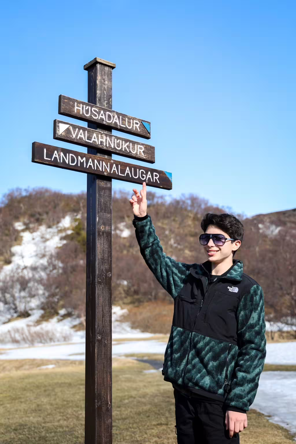 Young traveler pointing at Landmannalaugar trail signpost under clear blue sky on Iceland highland adventure