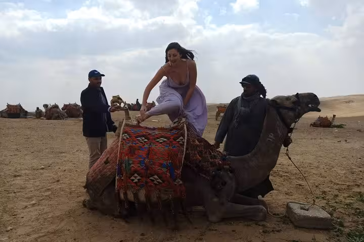 Traveler mounting a camel in Giza desert camp, private pyramids and Sphinx tour with camel ride and quad bike