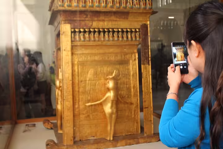 Traveler photographing golden artifact at Egyptian Museum Cairo, optional Tutankhamun’s mask tour add-on