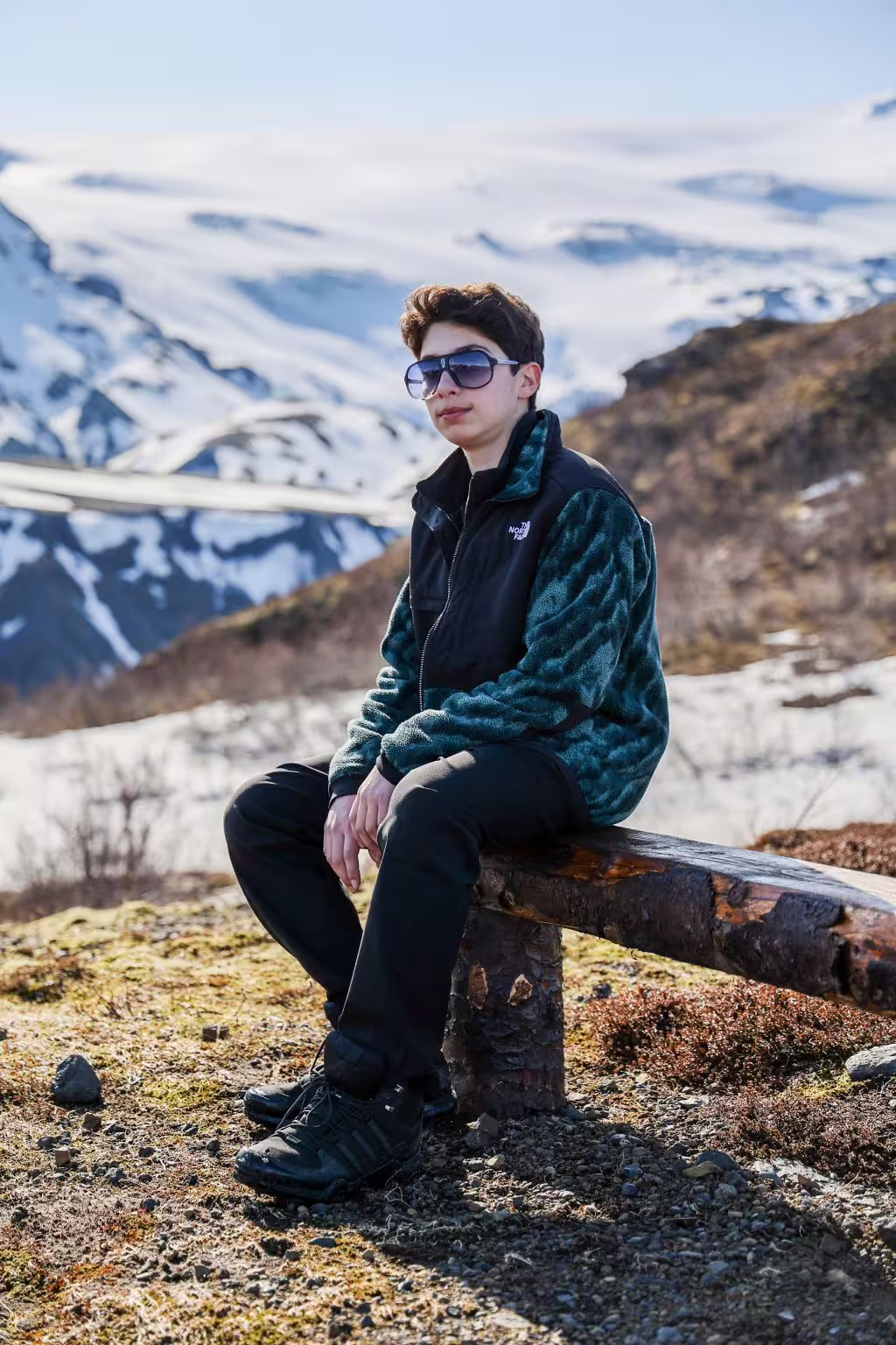 Young traveler resting on a wooden bench with stunning snowy glacier highlands in the background on a summer adventure tour.
