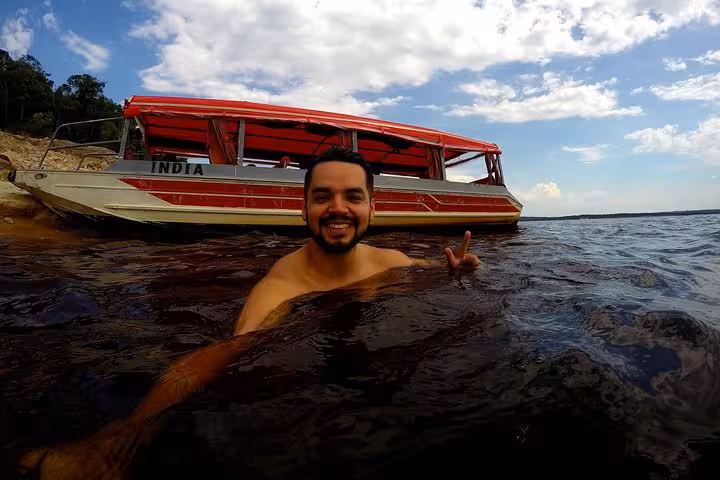 Traveler swimming in Rio Negro beside boat on 8-hour Amazonas jungle trek and Anavilhanas Archipelago tour