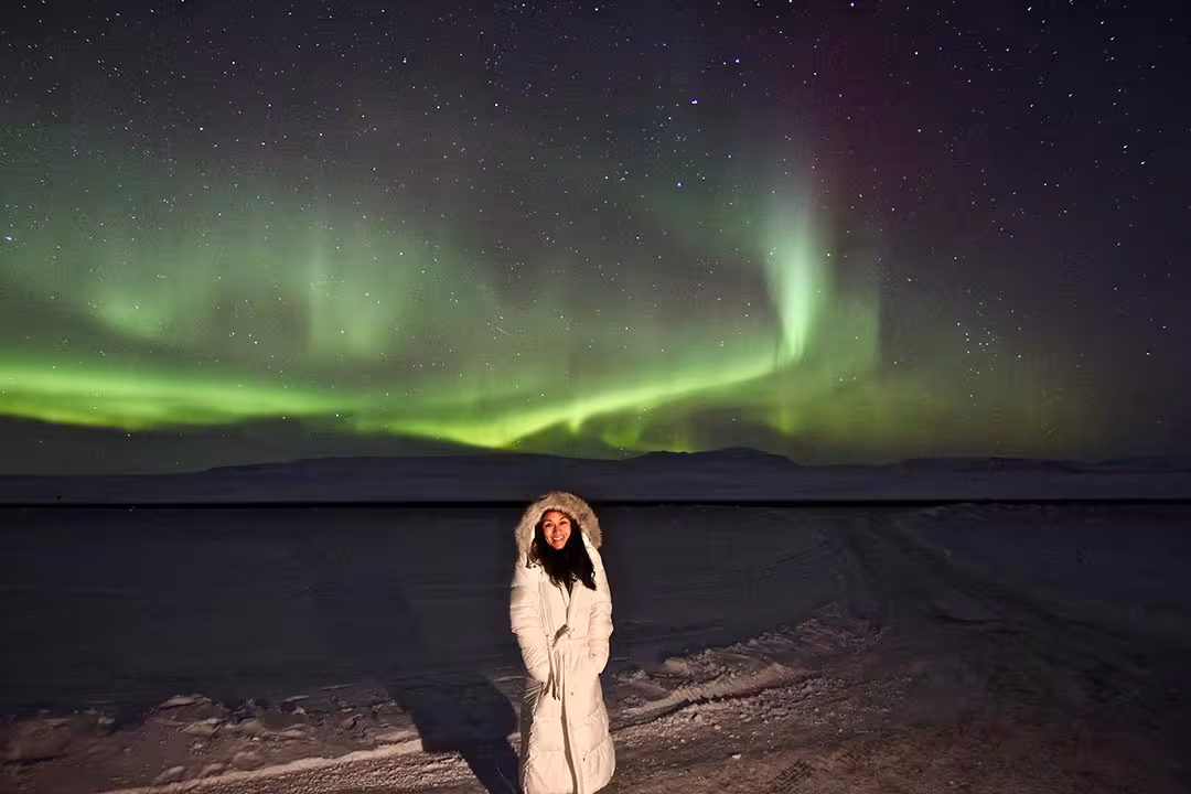 Traveler in white parka under green aurora borealis, winter northern lights and stargazing night tour photo